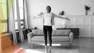 A black and white photo of a person standing in front of a sofa smiling.