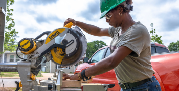 An African American woman wearing a green hard hat performing construction work