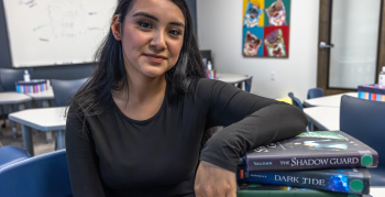 A smiling woman sitting in a classroom with her arm on a stack of books