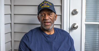 An African American male wearing a U.S. Navy hat sitting on a porch